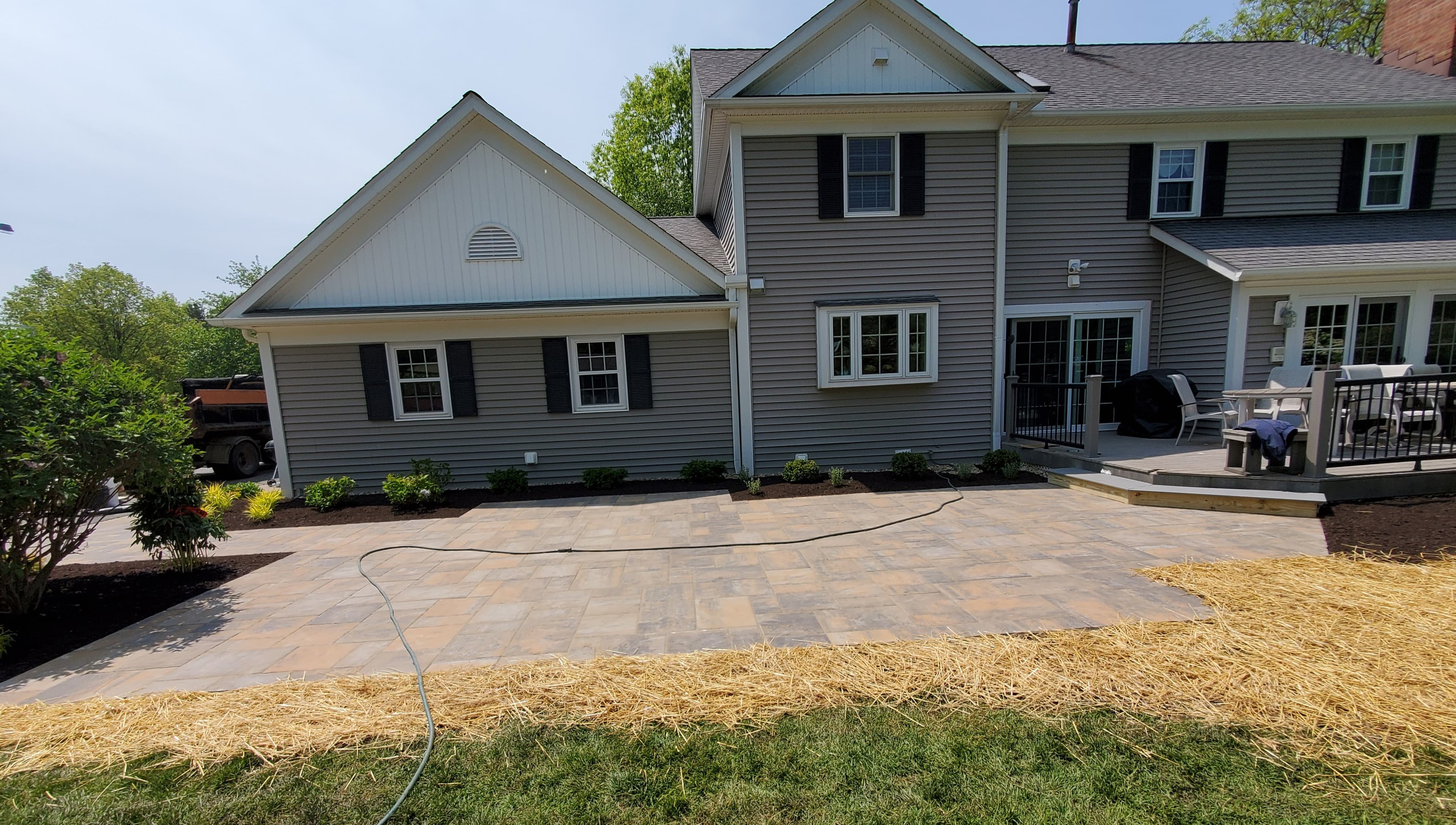 Large stone paver patio behind a gray house with white trim and fresh landscaping.