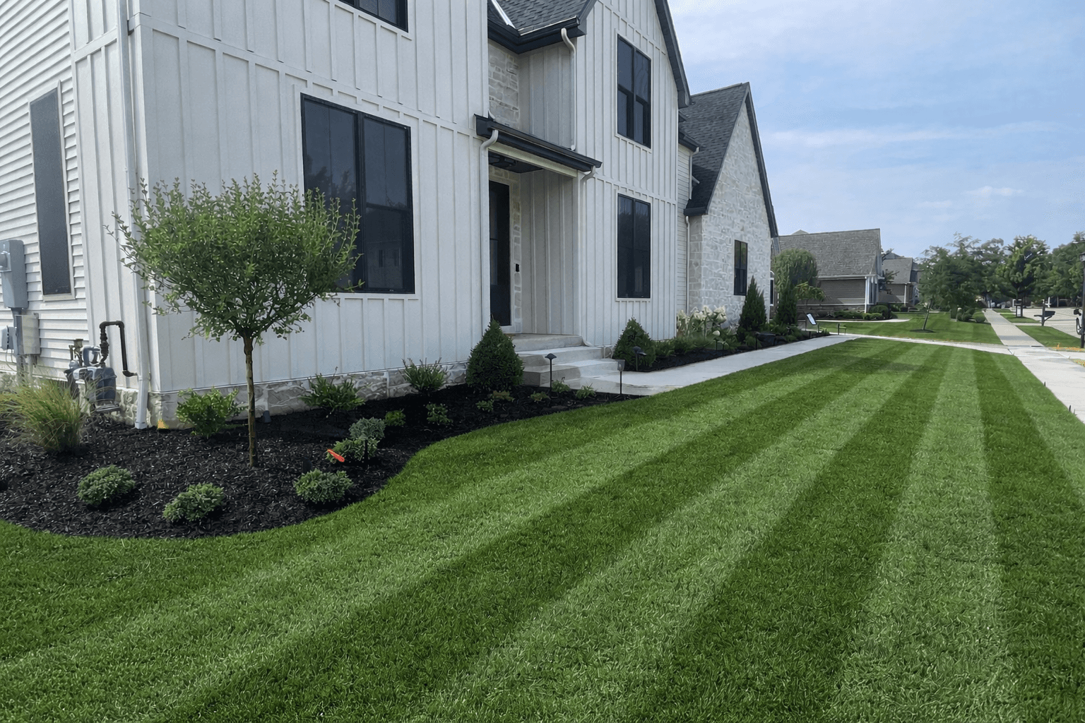 Modern white farmhouse with black windows and a perfectly manicured, striped green lawn.