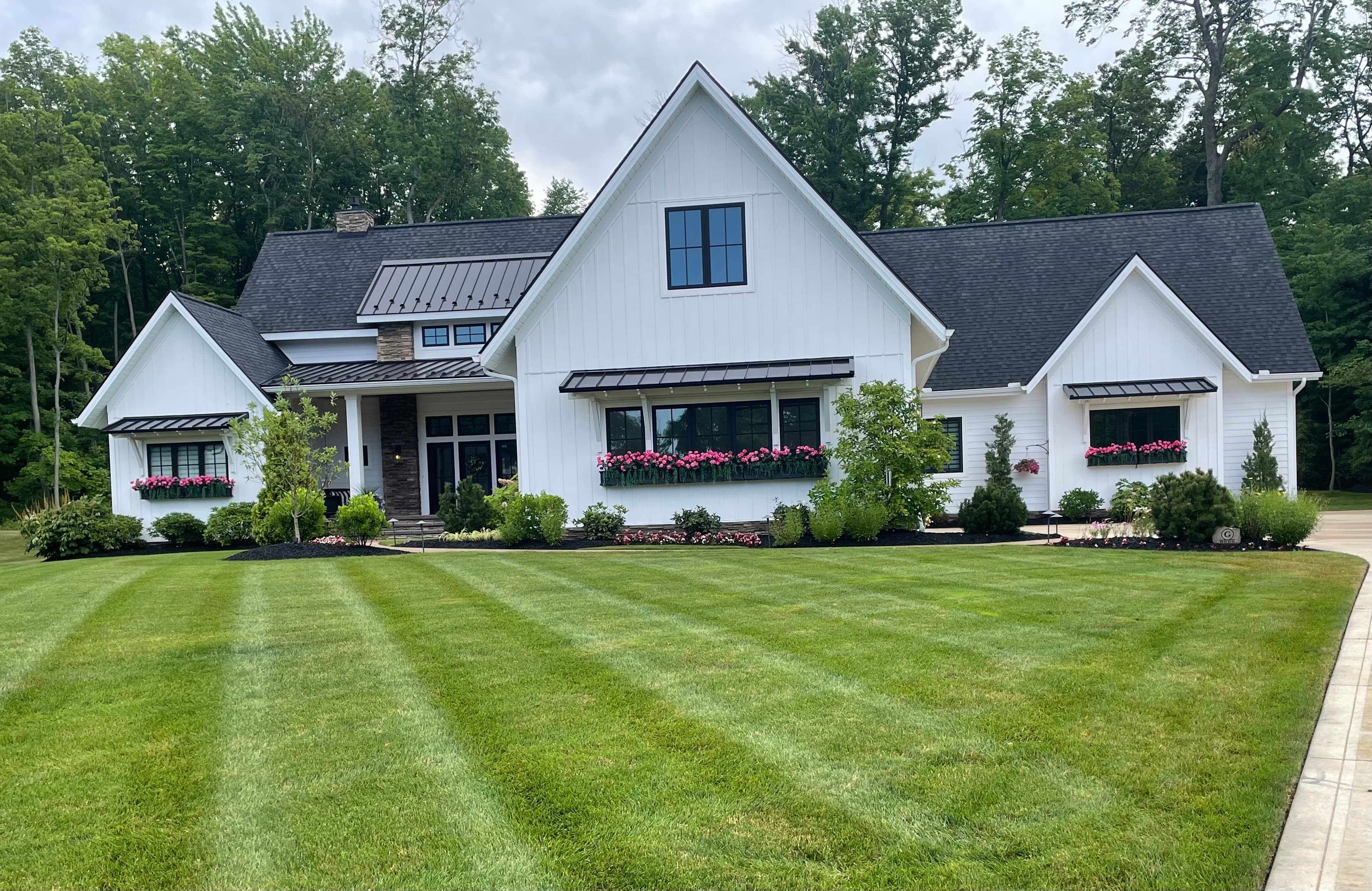 Modern white farmhouse with black accents, pink flower boxes, and a striped green lawn.