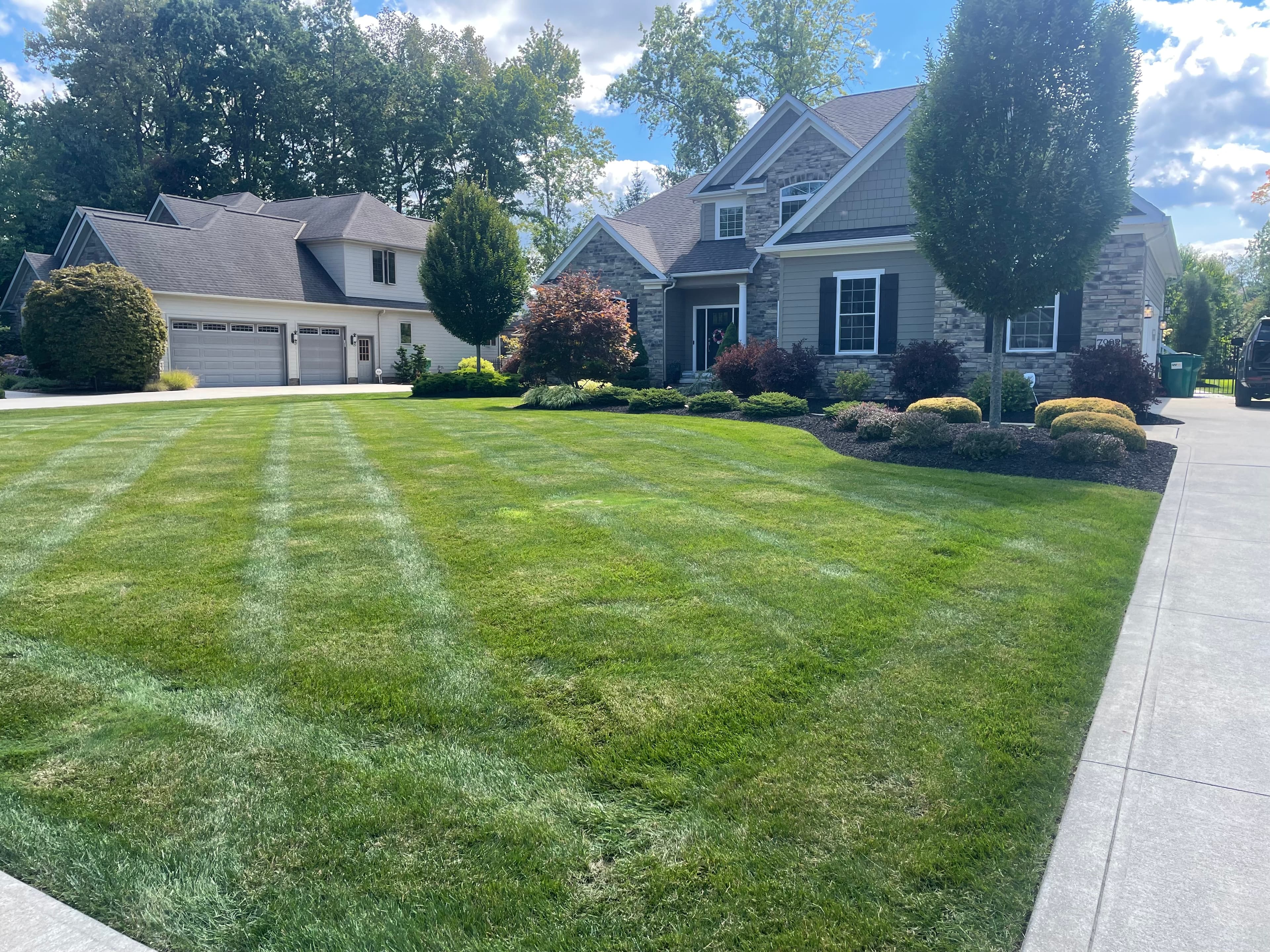 Modern suburban home with stone accents and a lush, professionally mowed striped green lawn.