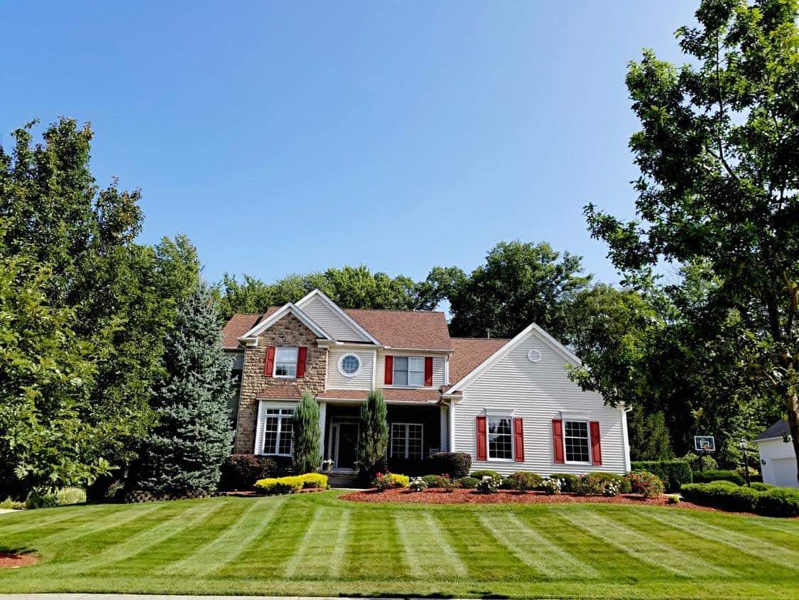 Suburban house with red shutters and a perfectly manicured, striped green lawn under blue sky.